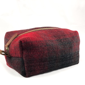 May include: A red and black plaid toiletry bag with a gold zipper and a brown leather pull tab.