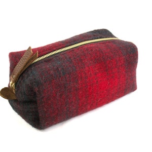 Könnte beinhalten: Eine rote und schwarze karierte Kosmetiktasche mit Reißverschluss und einem braunen Leder-Reißverschluss.