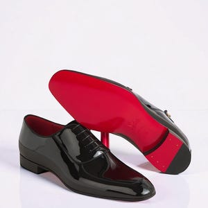 May include: A pair of black patent leather oxford shoes with a classic lace-up design. One shoe is positioned upright, while the other is tilted to reveal a vibrant red sole. The interior lining of the shoes is also a matching bright red colour.