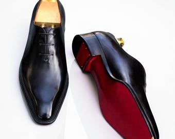 Nieuwe handgemaakte zwarte Oxford schoenen uit één stuk leer met rode leren zool.