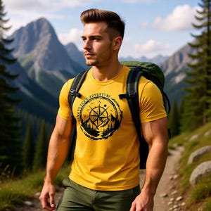 May include: A yellow t-shirt with a black compass design and the words "ALWAYS SEEK ADVENTURE" is worn by a person hiking on a mountain trail. The person is wearing a green backpack and olive green pants. Mountains and trees are in the background.