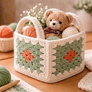 May include: A handmade crochet basket in cream, green, and orange, filled with yarn, a teddy bear, and flowers. The basket features a square design with a handle, perfect for storage or decoration.