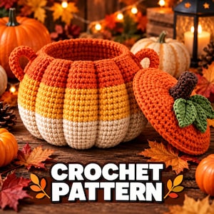 May include: A round, crocheted candy corn-themed basket with two side handles and a separate lid. The basket features horizontal stripes of orange, yellow, and cream. The lid is orange with a dark brown stem and two green crocheted leaves.