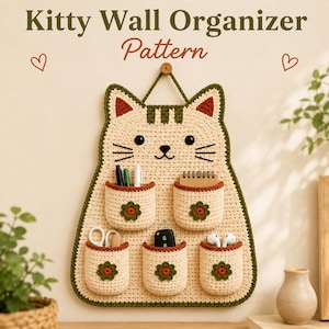 May include: A handmade, cream-colored cat-shaped wall organizer with six pockets. The organizer has a green and brown trim, with a wooden button for hanging. The pockets are filled with pens, scissors, and other small items. The text "Kitty Wall Organizer Pattern" is at the top.