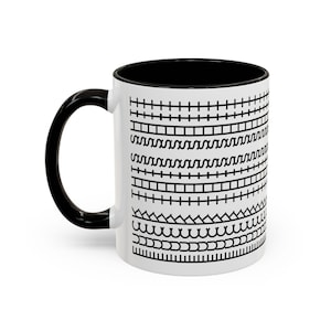 May include: White ceramic mug with a black interior and handle. The exterior has a repeating black pattern of geometric shapes and lines. The mug is suitable for hot or cold drinks.