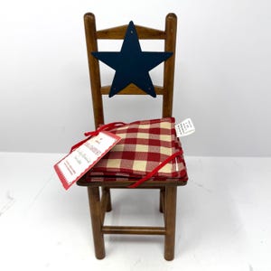 May include: A miniature wooden chair with a navy blue star on the back. The seat holds a stack of red and cream checkered coasters tied with a red ribbon. A red tag is attached to the coasters.