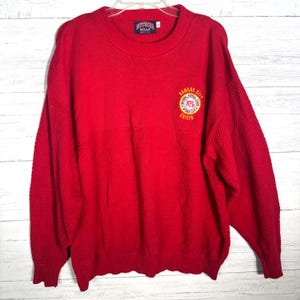 May include: A red sweater with the Kansas City Chiefs logo on the chest. The sweater has a textured design on the front and sleeves. The tag reads "NUTMEG" and "NFL".