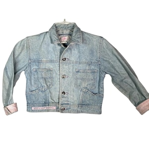 May include: A light blue denim jacket with a button closure and two front pockets. The jacket has a faded look and is cropped.