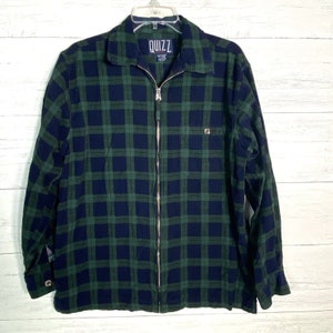 May include: A green and blue plaid long-sleeved shirt with a zipper closure and the word "QUIZZ" on the front.