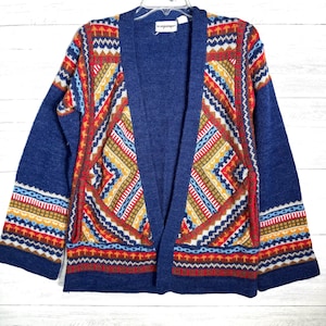 May include: A blue open-front cardigan with a colorful geometric pattern. The pattern includes red, yellow, white, and blue designs. The label reads "an original import".