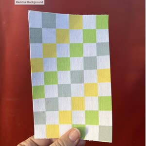 Puede incluir: Un trozo de papel rectangular con un patr&oacute;n de cuadros. El patr&oacute;n consiste en cuadrados alternos de color blanco, amarillo, verde claro y gris. El papel est&aacute; sostenido por una mano, y las palabras "Remove Background" est&aacute;n en la esquina superior izquierda.