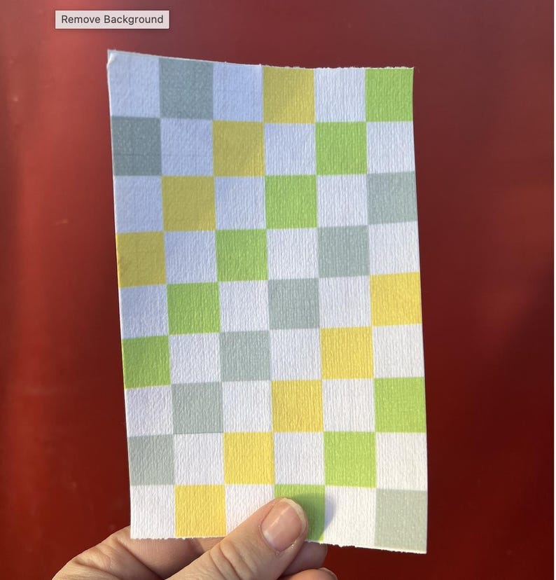 Puede incluir: Un trozo de papel rectangular con un patr&oacute;n de cuadros. El patr&oacute;n consiste en cuadrados alternos de color blanco, amarillo, verde claro y gris. El papel est&aacute; sostenido por una mano, y las palabras "Remove Background" est&aacute;n en la esquina superior izquierda.