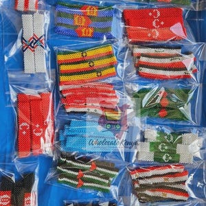 May include: A selection of beaded bracelets, packaged in clear plastic. The bracelets showcase diverse patterns in colours such as red, white, green, blue, and yellow. Some have geometric designs, others display symbols. The text "Wholesale Kenya" is visible.