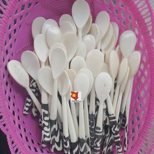 Può includere: Una collezione di cucchiai bianchi con coppette a forma di cuore e manici a fantasia bianchi e neri, esposti in un cestino rosa intrecciato. I cucchiai sono realizzati in un materiale chiaro.