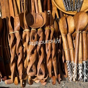 May include: A collection of handcrafted wooden kitchen utensils, including spoons, ladles, and serving forks. Some utensils feature intricate carved designs and zebra-striped patterns. The text "Africancrafts" is visible on some of the utensils.