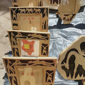 May include: Wooden picture frames with carved animal silhouettes, including giraffes, cheetahs, and elephants. The frames are light brown with dark brown accents. One frame has the text "5 x 7". The frames are displayed on a dark surface.