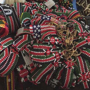 May include: A collection of beaded accessories in red, black, green, and white. The items appear to be bracelets and other jewelry, with intricate patterns and designs. Some pieces have a floral motif.