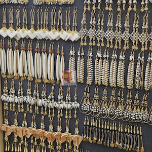 Puede incluir: Exhibición de varios pendientes hechos a mano. Los pendientes presentan diversos diseños, incluyendo formas geométricas, patrones de plumas y elementos de madera. Se incorporan detalles y cuentas de metal dorado, creando un surtido visualmente rico.