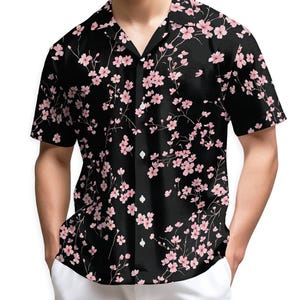 Puede incluir: Camisa negra de manga corta con un estampado floral de flores de cerezo rosas. La camisa tiene un cuello clásico y botones blancos. La camisa se combina con pantalones blancos.