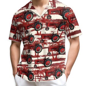 Puede incluir: Una camisa de manga corta con un estampado repetido de tractores rojos sobre un fondo crema con rayas rojas y siluetas de palmeras. Los tractores tienen neumáticos negros y ruedas rojas. La camisa tiene un cuello clásico.