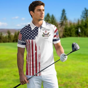 May include: A white polo shirt featuring a distressed American flag print on the left side, a United States of America emblem with an eagle and the text 1776-2026 on the chest, and small flag graphics on the sleeves with the year 2026 printed below.