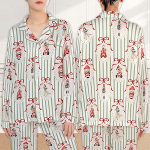 May include: A long-sleeved button-down pajama top with a notched collar, featuring a vertical light green and white striped pattern. The fabric is decorated with a repeating print of nutcracker figures and holiday ornaments with red bows.
