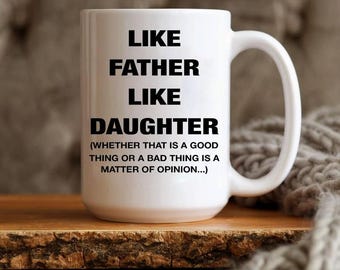 May include: White ceramic mug with the text "LIKE FATHER LIKE DAUGHTER" in black, with a humorous disclaimer. The mug has a large handle and sits on a wooden surface.
