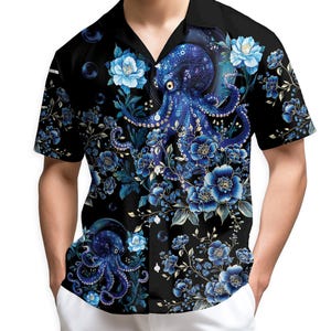 Puede incluir: Camisa negra de manga corta con un diseño de pulpo azul y floral. El diseño de la camisa presenta una ilustración detallada de un pulpo azul entre flores y follaje azules, sobre un fondo negro, creando un contraste llamativo.