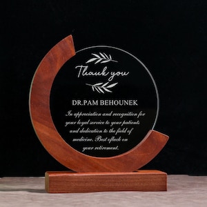 Könnte beinhalten: Eine Auszeichnung aus klarem Glas mit einem Holzsockel und Rahmen. Der Text "Thank you" und eine Widmung an Dr. Pam Behounek sind auf dem Glas eingraviert. Ein Ruhestandsgeschenk.