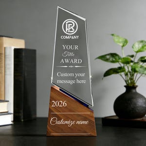 May include: A clear glass award with a wooden base. The award has text that reads "COMPANY", "YOUR Title AWARD", and "Custom your message here". The base has the year "2026" and the words "Customize name".