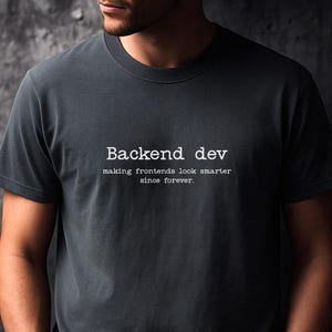 May include: Graphite gray t-shirt with the text "Backend dev making frontends look smarter since forever" in white. The shirt is a crew neck style and has short sleeves. The word "Graphite" is printed in the bottom right corner.