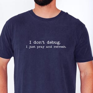 Könnte beinhalten: Marineblaues T-Shirt mit dem weißen Text: "I don't debug. I just pray and refresh." Das Shirt ist ein kurzärmeliges Rundhals-T-Shirt.
