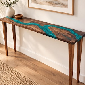May include: A long, narrow console table featuring a natural dark wood slab with a prominent, winding inlay of translucent turquoise resin running through the center. The table is supported by four tapered wooden legs and has a smooth, polished finish.
