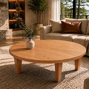 Könnte beinhalten: Ein runder Couchtisch aus hellbraunem Holz mit vier stabilen, konisch zulaufenden Beinen. Der Tisch hat eine glatte, kreisförmige Oberfläche mit sichtbarer Holzmaserung und steht niedrig, was eine stabile Ablagefläche bietet.
