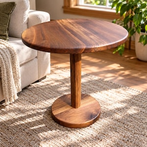 May include: A round side table crafted from dark brown wood with a smooth, circular tabletop, a single thick cylindrical central support column, and a flat, circular base that provides stability for the entire structure.