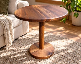 May include: A round side table crafted from dark brown wood with a smooth, circular tabletop, a single thick cylindrical central support column, and a flat, circular base that provides stability for the entire structure.