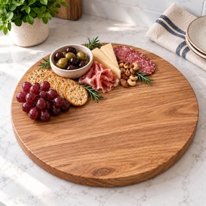 May include: A round wooden serving board featuring a selection of food items including a small bowl of green and black olives, sliced cheese, folded prosciutto, salami, a cluster of red grapes, round crackers, and a small pile of mixed nuts.