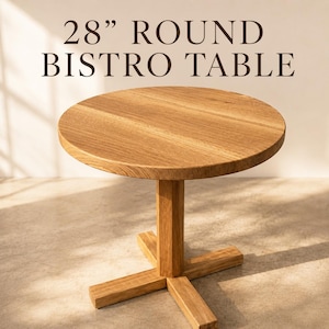 May include: A round bistro table made of light brown wood with a visible grain pattern. The table features a central vertical support column connected to a cross-shaped base. The text 28" ROUND BISTRO TABLE is displayed above the furniture piece.