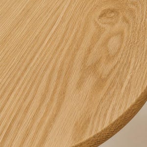 May include: A circular wooden tabletop featuring a light tan color and a prominent natural grain pattern. The surface displays a distinct wood knot and a smooth, rounded edge, showcasing the organic texture and warm tones of the light oak wood.