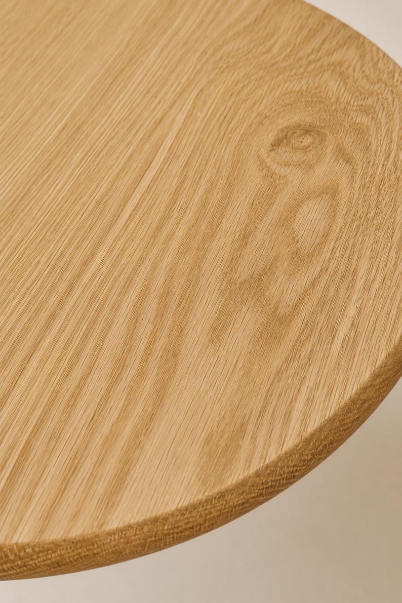 May include: A circular wooden tabletop featuring a light tan color and a prominent natural grain pattern. The surface displays a distinct wood knot and a smooth, rounded edge, showcasing the organic texture and warm tones of the light oak wood.