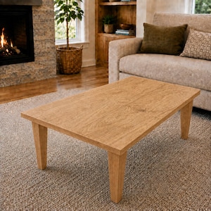 Peut inclure: Une table basse rectangulaire avec une finition en grain de bois brun clair, dotée d'un plateau plat et de quatre pieds droits légèrement effilés. La table est fabriquée en bois et présente une couleur brun clair naturelle et uniforme.