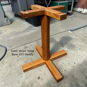 May include: A solid wood table base, DIY ready, with a cross-shaped top and base. The table base is made of light brown wood and is designed for easy assembly. The text "Solid Wood Table Base DIY Ready" is visible.