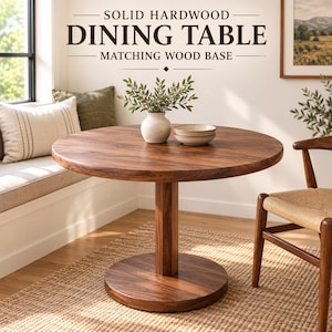 May include: A round solid hardwood dining table with a matching wood base. The table features a smooth, dark brown wood grain surface. Text above the table reads: SOLID HARDWOOD DINING TABLE MATCHING WOOD BASE. The table is set with a white vase and bowls.