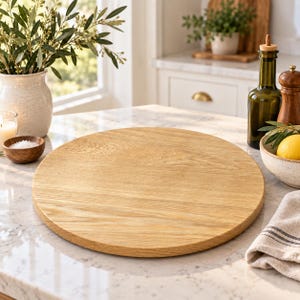 May include: A round, light-colored wooden serving board with a visible natural grain pattern. The circular board features a smooth, flat surface and is positioned centrally, showcasing its simple, functional design and warm, organic wood tone.