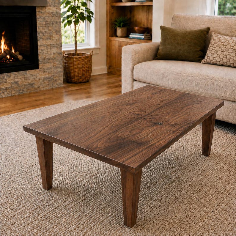 K&ouml;nnte beinhalten: Ein rechteckiger Couchtisch aus dunkelbraunem Holz mit einer glatten, flachen Oberfl&auml;che und vier stabilen, leicht konisch zulaufenden Beinen. Der Tisch weist eine sichtbare nat&uuml;rliche Holzmaserung auf der Oberseite auf.