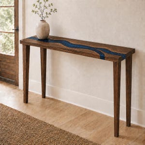 May include: A rectangular wooden console table with four tapered legs and a natural brown finish. The tabletop features a central, winding inlay of deep blue resin that runs horizontally across the surface. A beige ceramic vase sits on top.