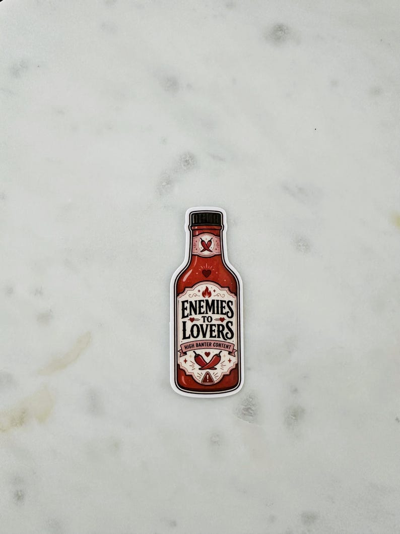 May include: A die-cut sticker shaped like a hot sauce bottle with a red label. The text reads ENEMIES TO LOVERS and HIGH BANTER CONTENT. The design features illustrations of chilli peppers, small hearts, and a flame icon on a red background.