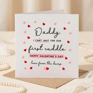 Puede incluir: Tarjeta blanca de San Valentín con el texto "Daddy, I can't wait for our first cuddle, Happy Valentine's Day, love from the bump." Decorada con corazones rojos y rosas.