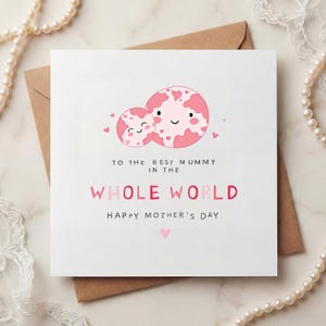 May include: A white Mother's Day card with a brown envelope. The card features two pink planet-like figures with heart-shaped details and the text "TO THE BEST MUMMY IN THE WHOLE WORLD HAPPY MOTHER'S DAY".