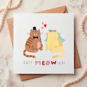 May include: A square wedding card featuring two cartoon cats. One cat is brown with a black top hat and bow tie, the other is yellow with a floral crown and veil. The text "JUST MEOWIED!" is below the cats.